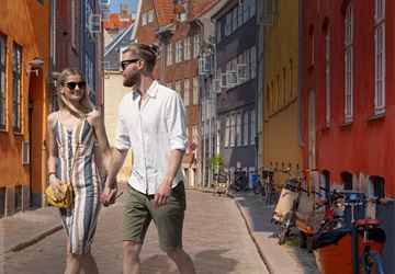 En dame og mand der holder i hånden og går tur i brostensgade med farverige bygninger - 24 timer i byen