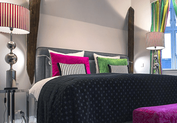 Hotelværelse med dobbeltseng med sort sengetæppe og farverige puder - Parkering Hotel Absalon