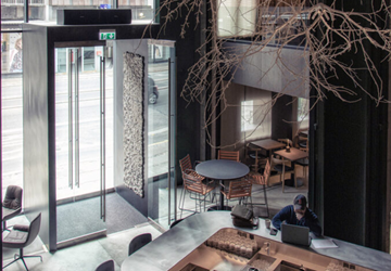 Moderne hotel lounge med høj glasdør, borde og en person der arbejder på bærbar computer - Herman k lounge