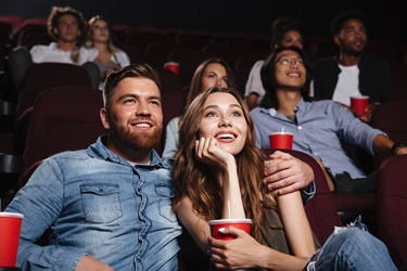 People watching a movie in a cinema, two individuals sitting close together holding drinks