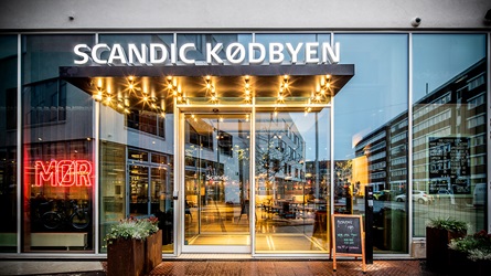Indgang til Scandic Kødbyen med glasdøre, skilt og neonbelysning i bymiljø - Parkering Q-Park Scandic Kødbyen