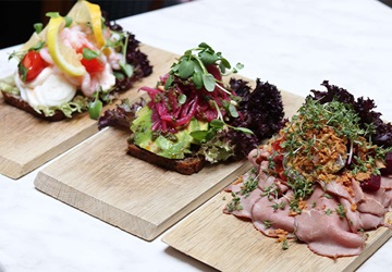 Three pieces of traditional Danish smørrebrød (open-faced sandwiches) on wooden boards with egg, vegetables, meat, and crispy toppings - Zirup