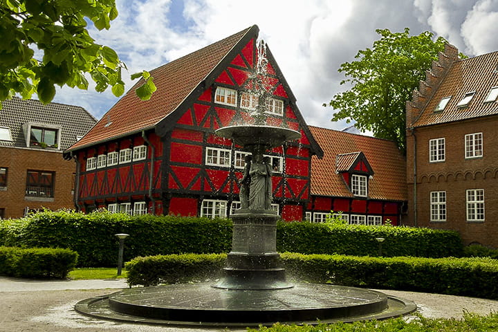 Rødt bindingsværk i Aalborg med springvand i forgrunden