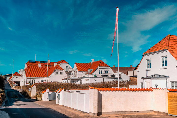 Blokhus by med hvide huse med røde tag og flag blafrende ved blå himmel