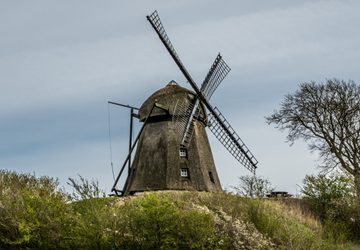 Havnø Mølle in Hadsun in black, raised on a green hill against a grey sky