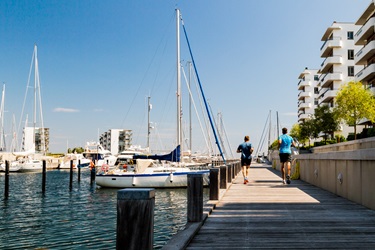 Hellerup harbour in the sunshine. Two people run past yachts on the water