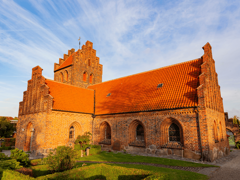 Herlev Kirke i solen. Rød mursten og rødt tag