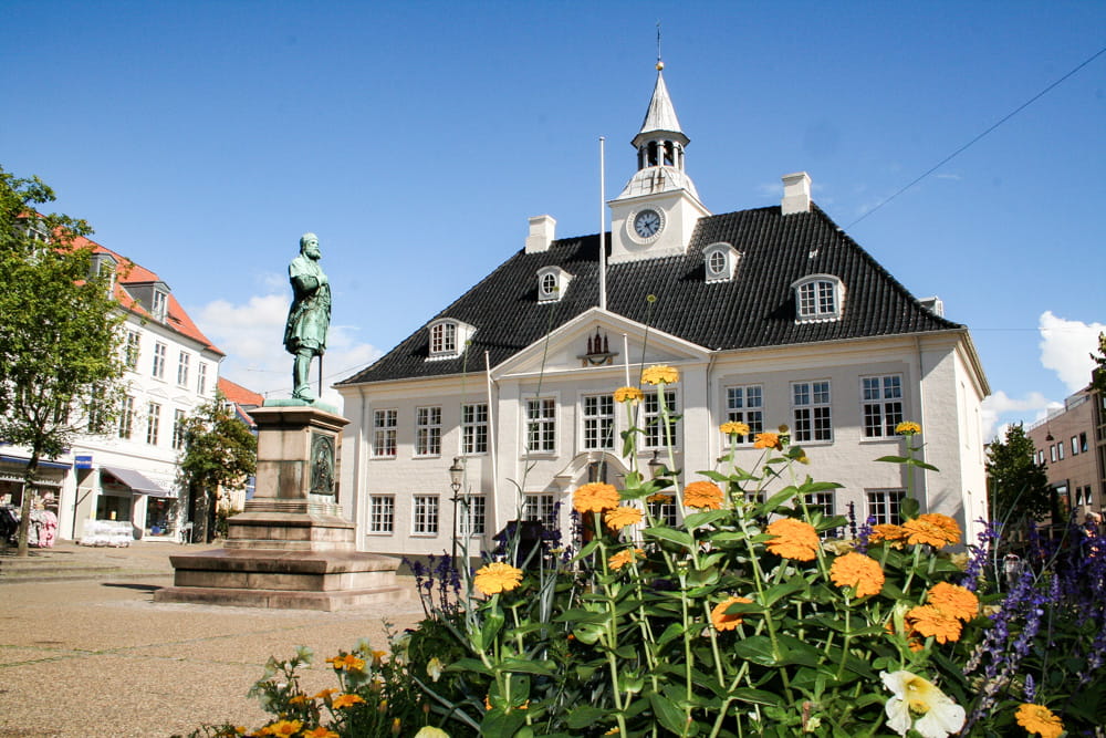 Randers Rådhus på en flot sommerdag. Foran Rådhuset står en statue af Niels Ebbesen