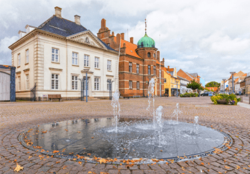 Stege by med gamle bygninger og springvand i forgrunden