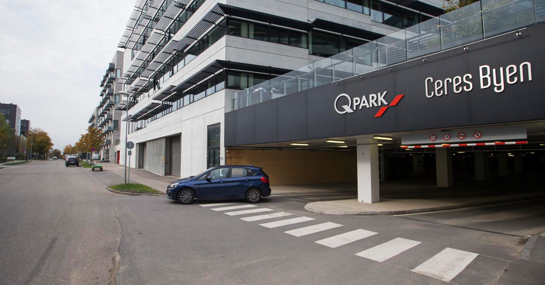 Q-Park Ceres Byen seen from the outside of a black and white building and a blue car exiting the facility