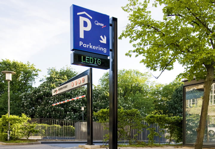 Q-Park Nørreport indkørsel med skilt i forgrunden og grønne træer bagved.